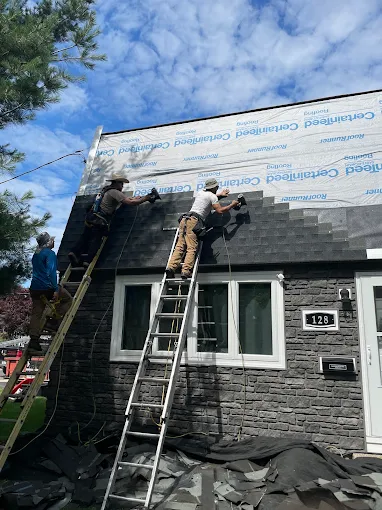 Roofers on ladders fastening new shingles over underlayment
