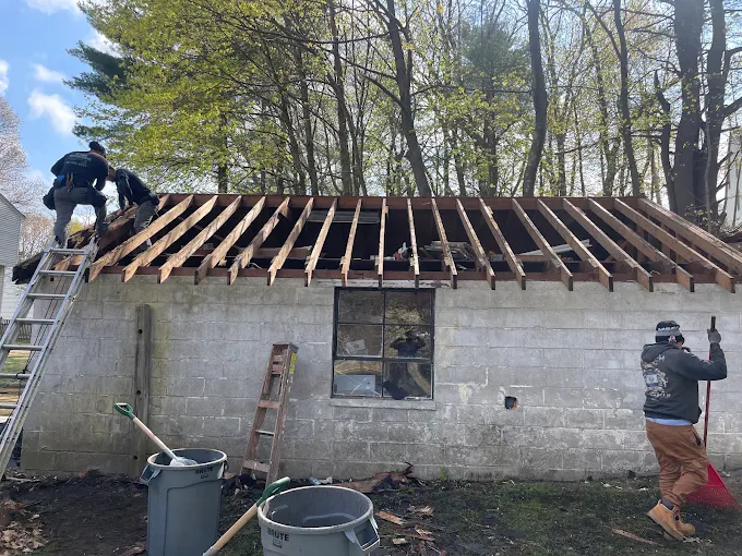 Crew tearing off a garage roof in spring, rafters exposed