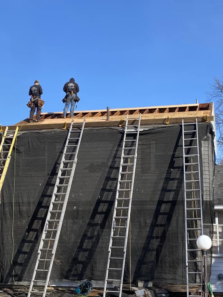 Two KMK roofers standing on an open roof deck, ladders set against the house