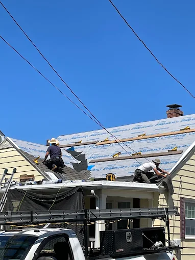 Two roofers installing shingles over underlayment on a sunny day