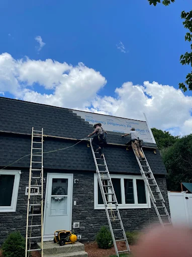 Roofers on ladders fastening shingles on a stone-front house